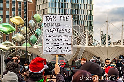 STRATFORD, LONDON, ENGLAND- 5 December 2020: Anti-lockdown Standupx protester holding a â€˜Tax the covid profiteersâ€™ placard Editorial Stock Photo